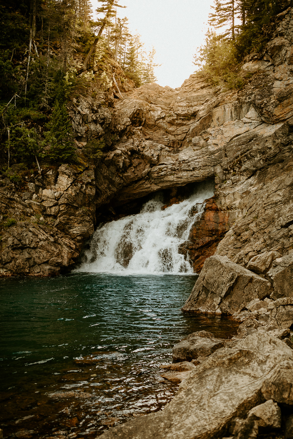 A waterfall in the Two Medicine region of Glacier National Park with the evening sunlight glistening behind it.